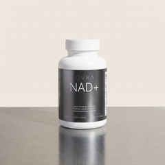 OVRA NAD+ bottle on brushed steel, bone-white studio background