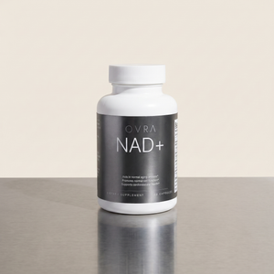 OVRA NAD+ bottle on brushed steel, bone-white studio background