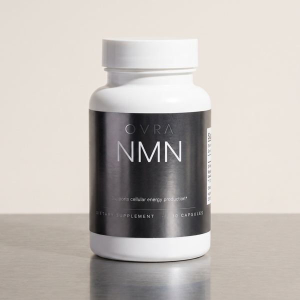 OVRA NMN bottle on brushed steel, bone-white studio background